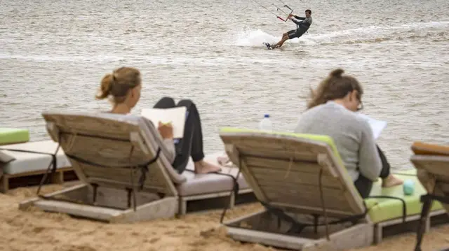 Deux vacanciers européens profitent de chaises longues au Sahara occidental tandis qu'un autre pratique le kitesurf en mer