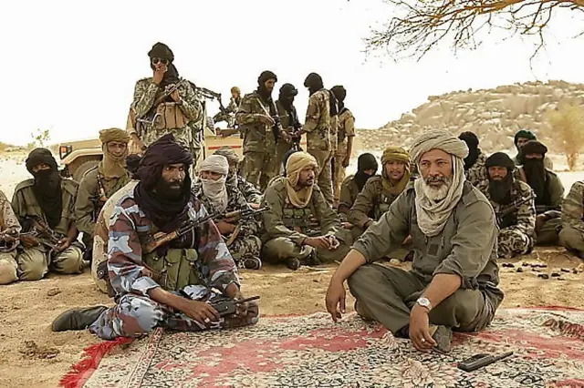 Combattants touaregs discutant sous un arbre dans le désert malien.