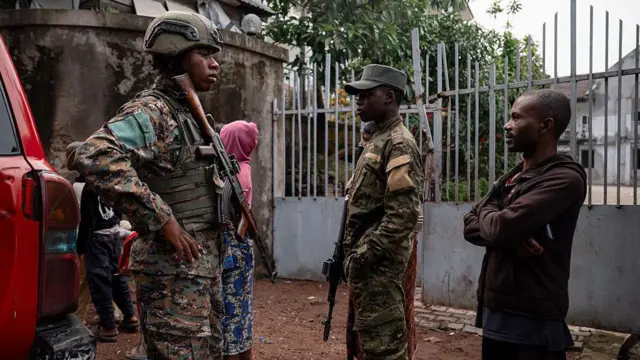 Deux militaires en uniforme aux côtés d’un civil et d’une femme en arrière-plan, illustration des tensions persistantes dans l’est de la RDC.